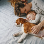 women, baby and puppy laying on bed sleeping