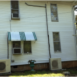 A typical U.S. style home is shown here with a retrofit mini-split system. Notice the exterior line sets and condensate drains. Thermal losses could be expected from the vertical, external refrigerant lines and these might cause the system to have trouble keeping up on really hot days. Also, notice that the window-room air conditioners have not yet been removed. 